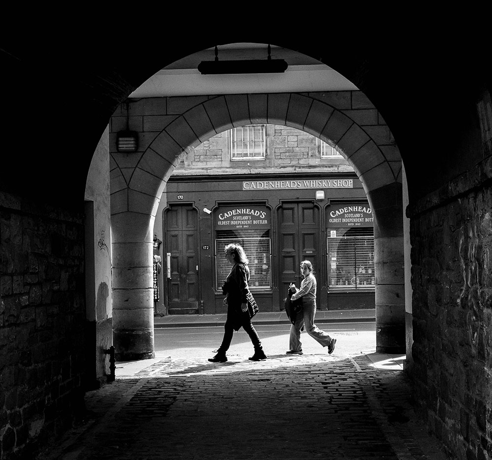 Black and white street photography of Edinburgh Royal Mile through a stone archway